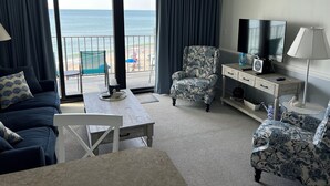 Habitación de hotel con balcón, televisión, escritorio y una silla.