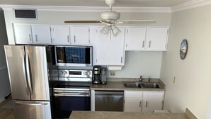 A compact kitchen with white cabinets, stainless steel appliances, and a wooden island with two chairs.
