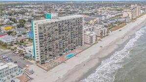 A high-rise hotel with multiple balconies, a swimming pool, and a beach view.