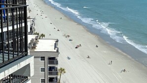 A beach with people sunbathing and swimming, a clear sky, and a view of the ocean.