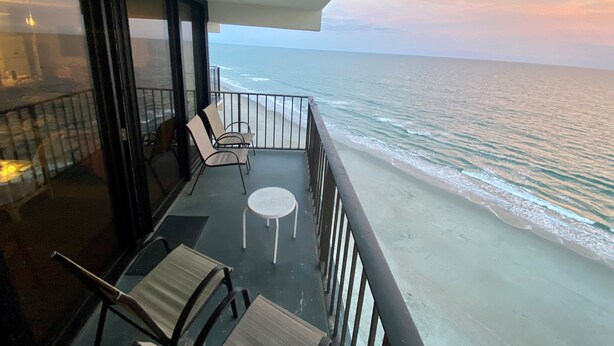 A balcony with a view of the ocean, featuring a table and chairs.