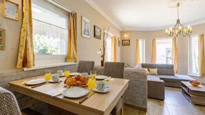 Un coin repas avec une table en bois mise pour le petit-déjeuner, un canapé et un lustre.