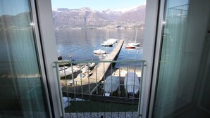 Vista desde un balcón sobre un puerto deportivo con barcos amarrados, un muelle que se adentra en el agua y montañas al fondo.
