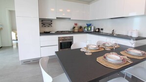 Una cocina moderna con armarios blancos, una estufa a gas y un comedor con platos y vasos.