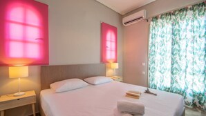 A hotel room with a large bed, two bedside lamps, an air conditioner, and a window with floral curtains. - Immaculate 1-Bed House in Zakynthos (Zakynthos)