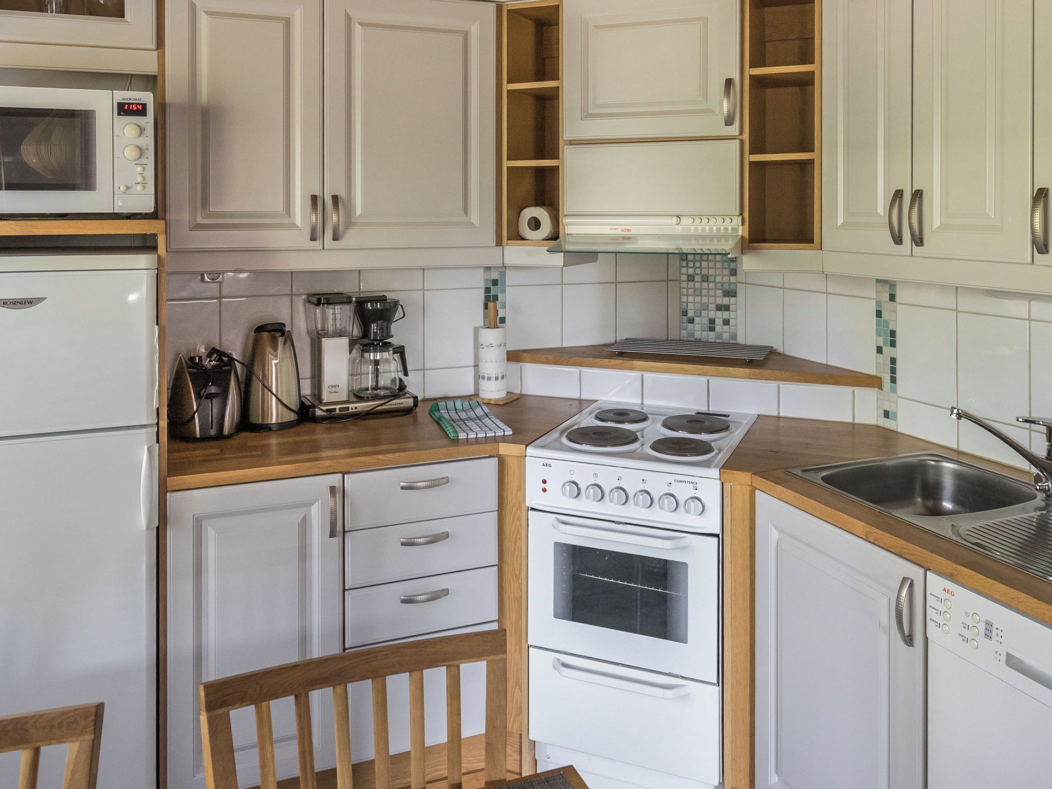 Una cocina compacta con gabinetes blancos, un microondas integrado, una cafetera y una estufa.