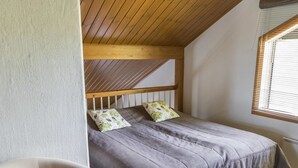 A small, cozy bedroom with a sloped ceiling, a single bed with a grey bedspread, two pillows, a wooden headboard, a window with blinds, and a chair. - Alppinuppu by Interhome (Nilsiä)