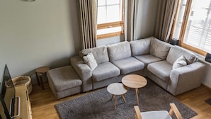 A modern living room with a grey sectional sofa, two small round tables, a grey rug, and a wooden floor. - Alppinuppu by Interhome (Nilsiä)
