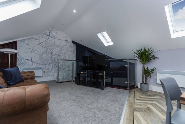A modern living room with a high ceiling, a large TV, a glass partition, a potted plant, and a sofa. - Luxury modern Loft apartment by Bootique (Wakefield)