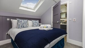 Una camera da letto con un velux, un letto con copriletto blu e bianco, e un bagno visibile attraverso una porta aperta.