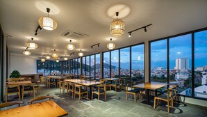 A spacious dining area with high tables and chairs, large windows offering a city view, and modern pendant lighting. - Aquatel Vung Tau (Ho Chi Minh City)