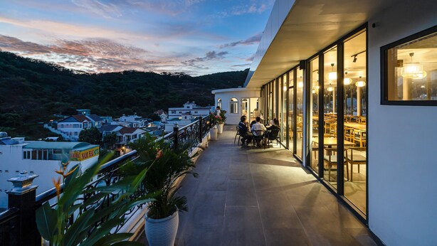 A balcony with a view of a hillside, potted plants, and a dining area with tables and chairs. - Aquatel Vung Tau (Ho Chi Minh City)
