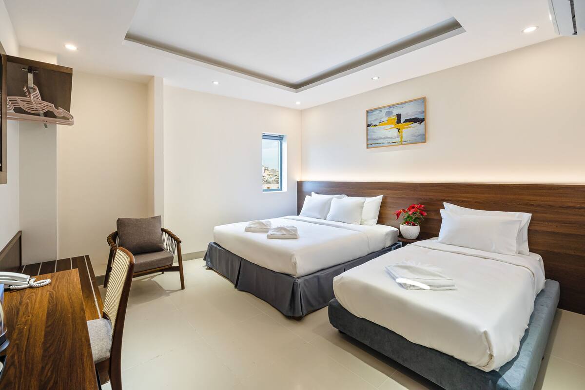 A hotel room with two beds, a desk with a telephone, a chair, a window, and a painting on the wall.
