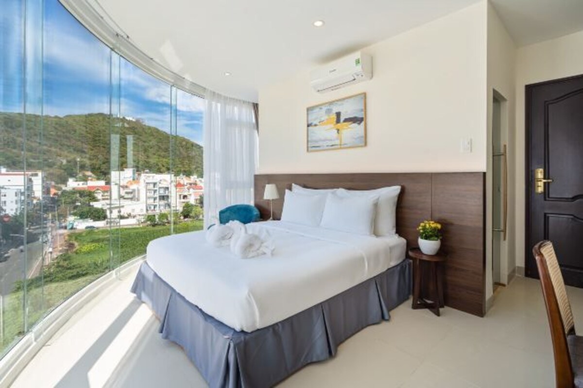 Habitación de hotel con una cama grande, vistas a la ciudad y un balcón.