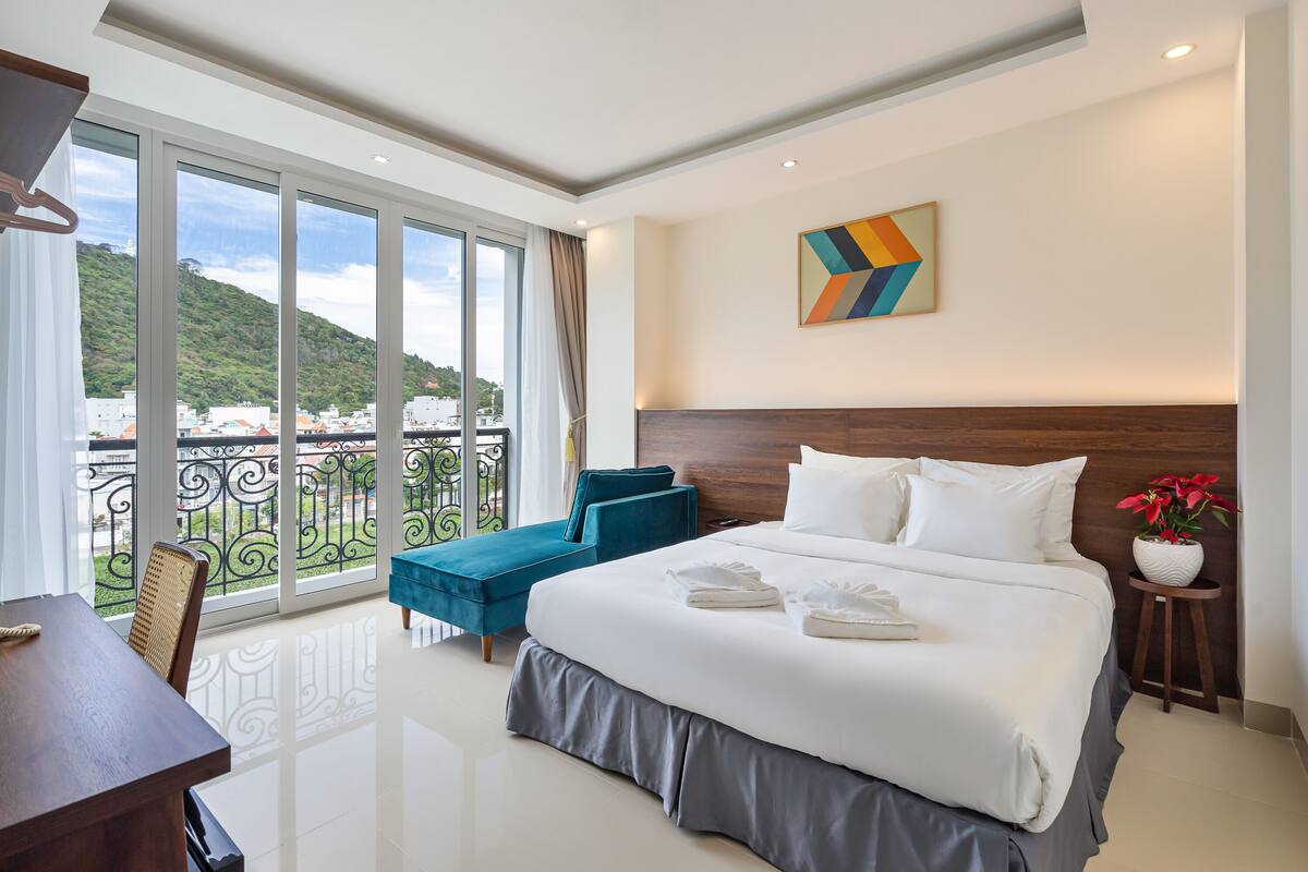 A hotel room with a large bed, a balcony with a view of the city, and a modern design.