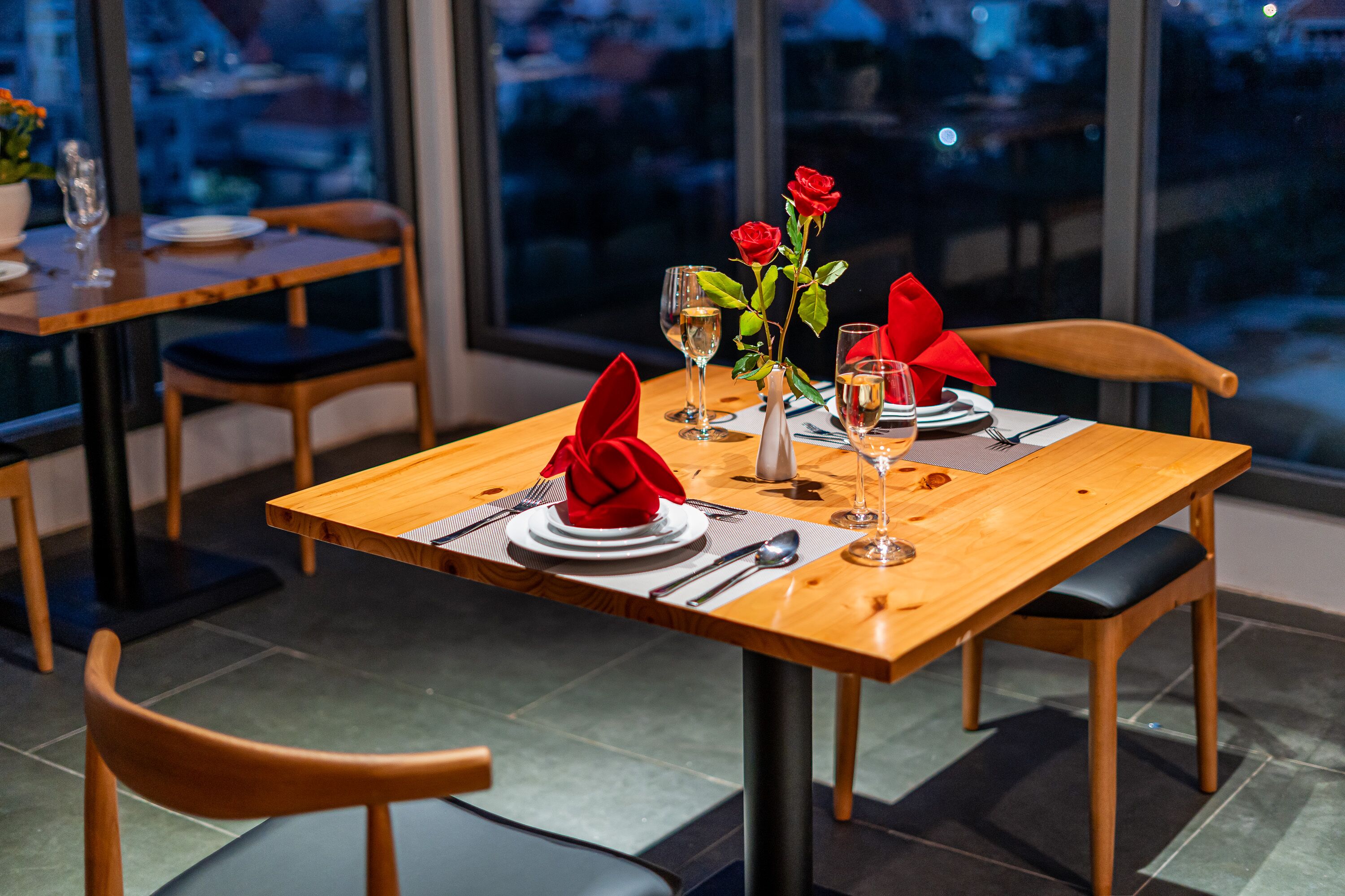 A dining table set with red napkins, wine glasses, and a vase with red roses.