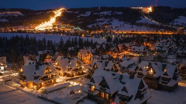 A snow-covered village with traditional chalet-style buildings, a ski lift in the background, and a lit ski resort area. - Lipki Park Resort by Interhome (Zakopane)