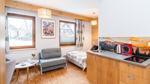 A compact living space with a kitchenette, a sofa, a small table, and a window with curtains. - Lipki Park Resort by Interhome (Zakopane)