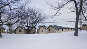 Fileira de casas térreas com o chão coberto de neve, cercada por árvores sem folhas.