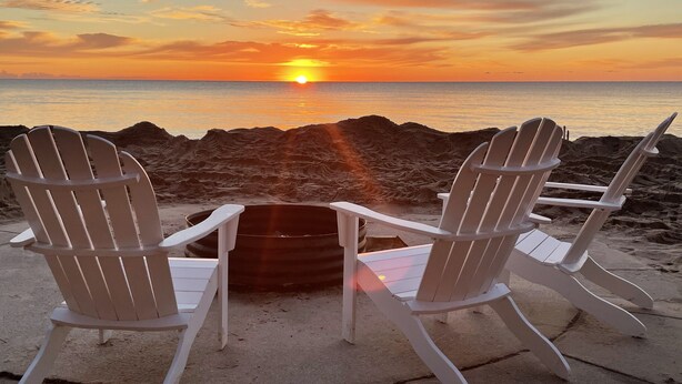Duas cadeiras Adirondack de frente para um pôr do sol sobre o oceano.