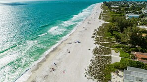 An aerial view of a beach with a long stretch of sand, a few people, and buildings in the background. - Beach Condo with Pool Near Holmes Beach! (Holmes Beach)