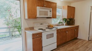 A kitchen with wooden cabinets, a white stove, and a microwave. - Tadpole Cottage (Cloverdale)