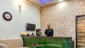 A reception area with a wooden reception desk, a television, a clock, and a wall with a textured pattern. - Hotel Walnut Creek (Nainital)