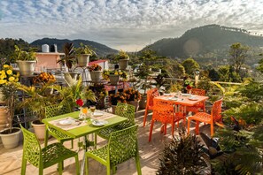 Una terraza en la azotea con mesas y sillas, rodeada de plantas y flores en macetas.