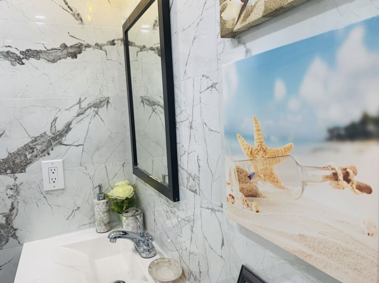 A bathroom with a marble sink, a mirror, and a beach-themed poster.
