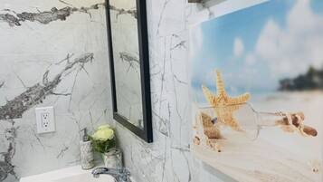 A bathroom with a marble sink, a mirror, and a beach-themed poster.