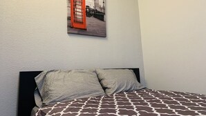 Una cama con una colcha estampada, dos almohadas y un cuadro en la pared de un teléfono rojo.