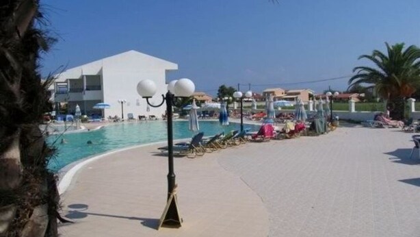 Un espace aménagé au bord de la piscine, avec des chaises longues, des parasols et un bâtiment en arrière-plan.