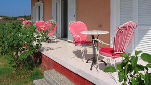 Une terrasse extérieure couverte, avec des chaises en métal rouge et blanc et une petite table ronde.