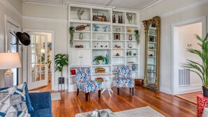 Un soggiorno con pavimento in legno, due poltrone a fantasia, un tavolino da caffè, una libreria piena di oggetti decorativi e un grande specchio.