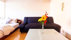A room with a bed, a dark-colored sofa, a white table, and a vase with flowers. - Commence3 (Sapporo)