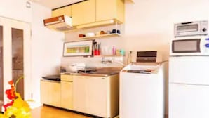 A kitchen with white cabinets, a microwave, and a refrigerator. There is a vase with flowers on the counter. - Commence3 (Sapporo)