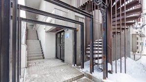 A gated entrance with a metal gate, a staircase leading to a building, and a snow-covered ground. - Commence3 (Sapporo)