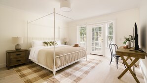 Um quarto com uma cama de dossel, uma escrivaninha de madeira, uma cadeira, um criado-mudo e um abajur.
