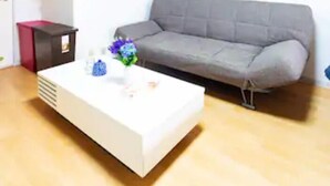 Un salon avec un canapé gris, une table basse blanche ornée d’un vase de fleurs et un meuble rouge.