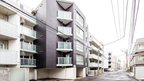 Un immeuble résidentiel à plusieurs étages, doté de balcons, d’une façade plane et situé dans une rue mouillée.
