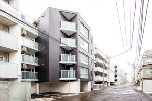 A multi-story residential building with balconies, a flat facade, and a wet street. - Commence4 (Sapporo)