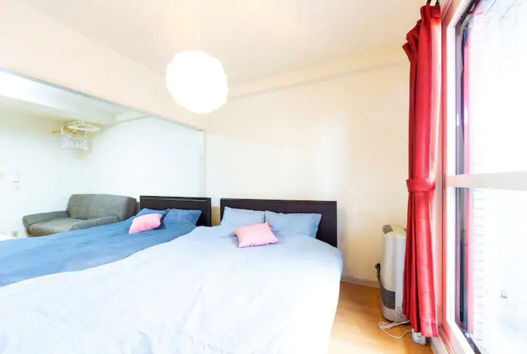 A room with two beds, a sofa, a heater, and a window with red curtains.