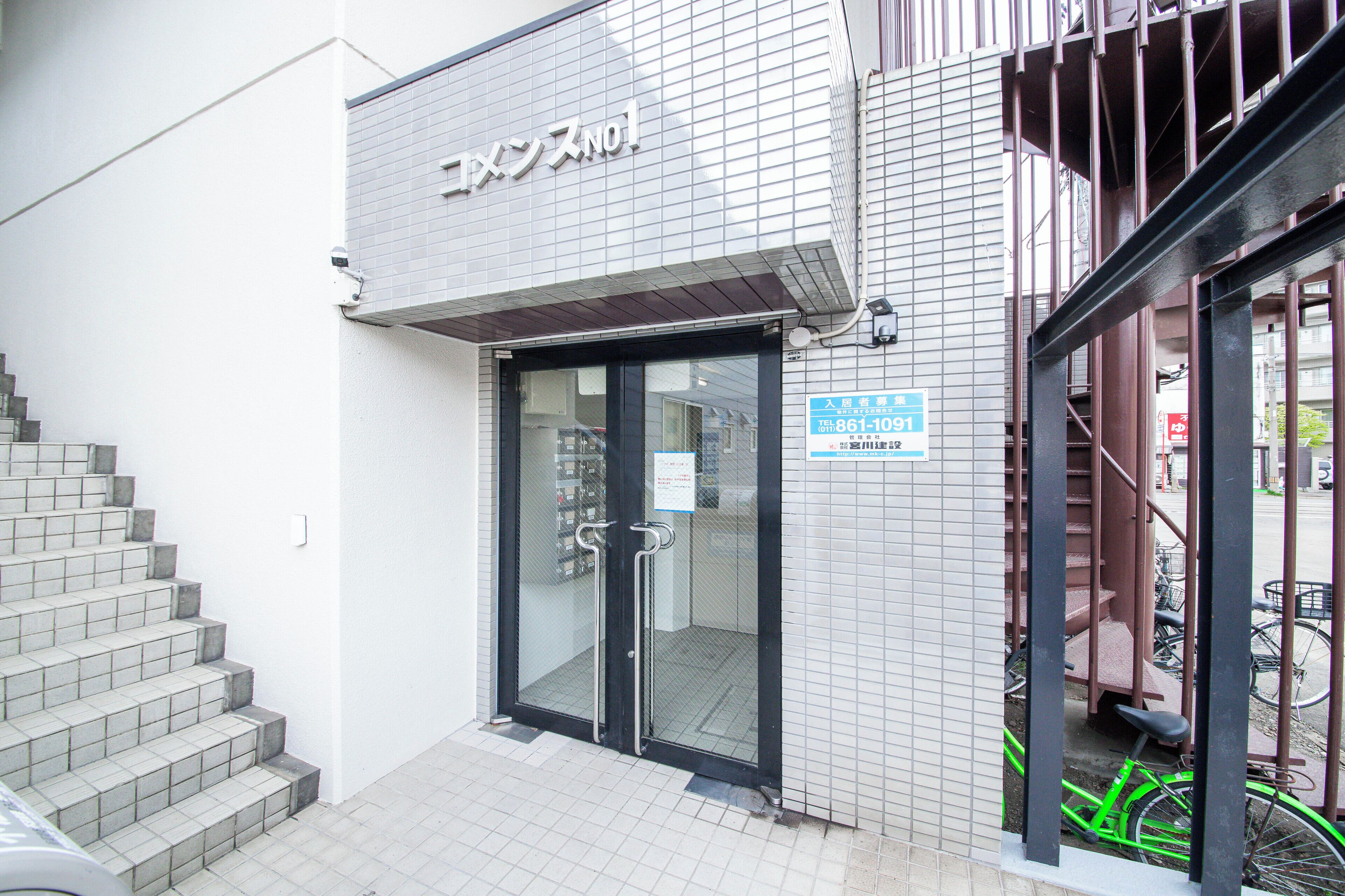 A building with a tiled exterior, a glass door entrance, and a staircase leading to the entrance.