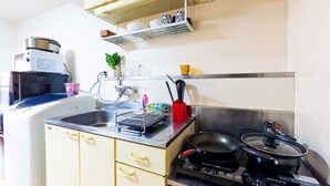 Une cuisine compacte équipée d’un évier, d’une cuisinière et d’un four à micro-ondes. On y trouve des placards, une étagère avec de la vaisselle et une plante en pot.