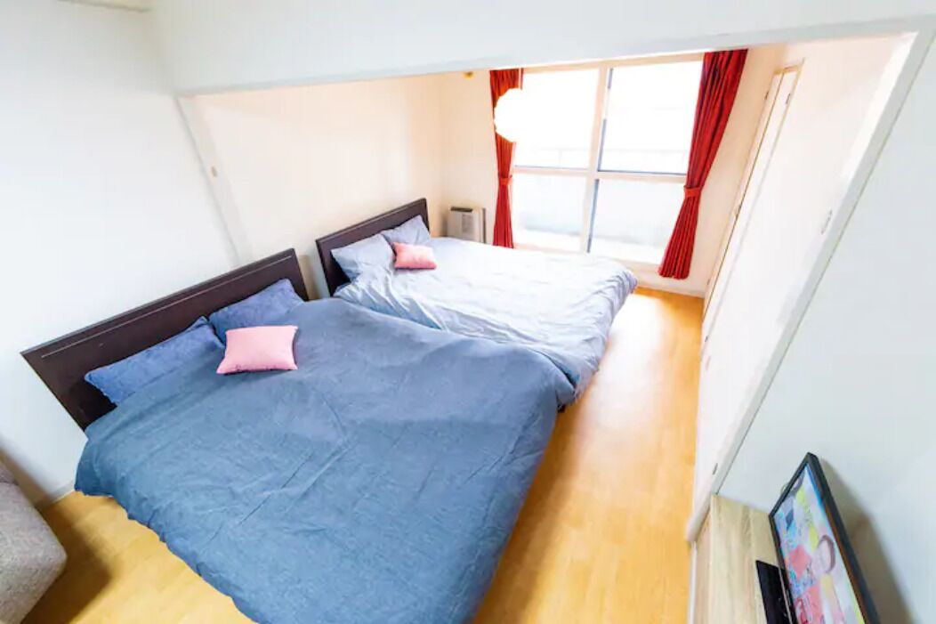 A room with two beds, a window with red curtains, and a small table.