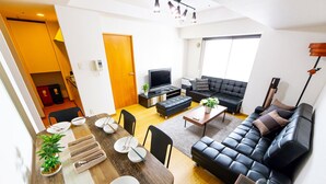 A modern living room with a black leather sofa, a wooden dining table set for four, and a TV. - Prime (Sapporo)