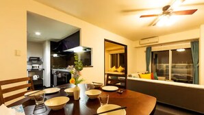 A dining area with a dark wooden table set for four, bowls, chopsticks, and a vase with flowers. A ceiling fan is visible above. - Fancy (Sapporo)