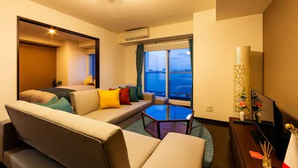 A modern hotel room with a sofa, a small table, and a view of the cityscape through large windows. - Fancy (Sapporo)