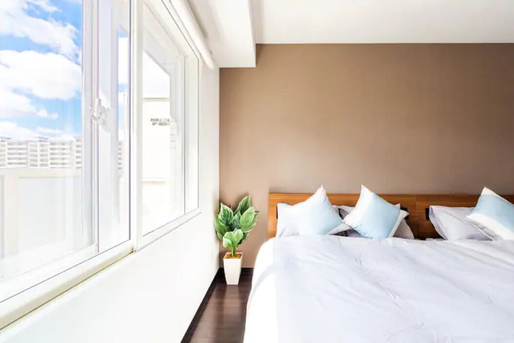 A hotel room with a large window, a bed with white bedding, and a potted plant. - Fancy (Sapporo)