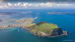 An aerial view of a coastal town with a prominent green hill, clear blue waters, and a distant island. - Hotel Golden Daisy Seogwipo Ocean (Seogwipo)